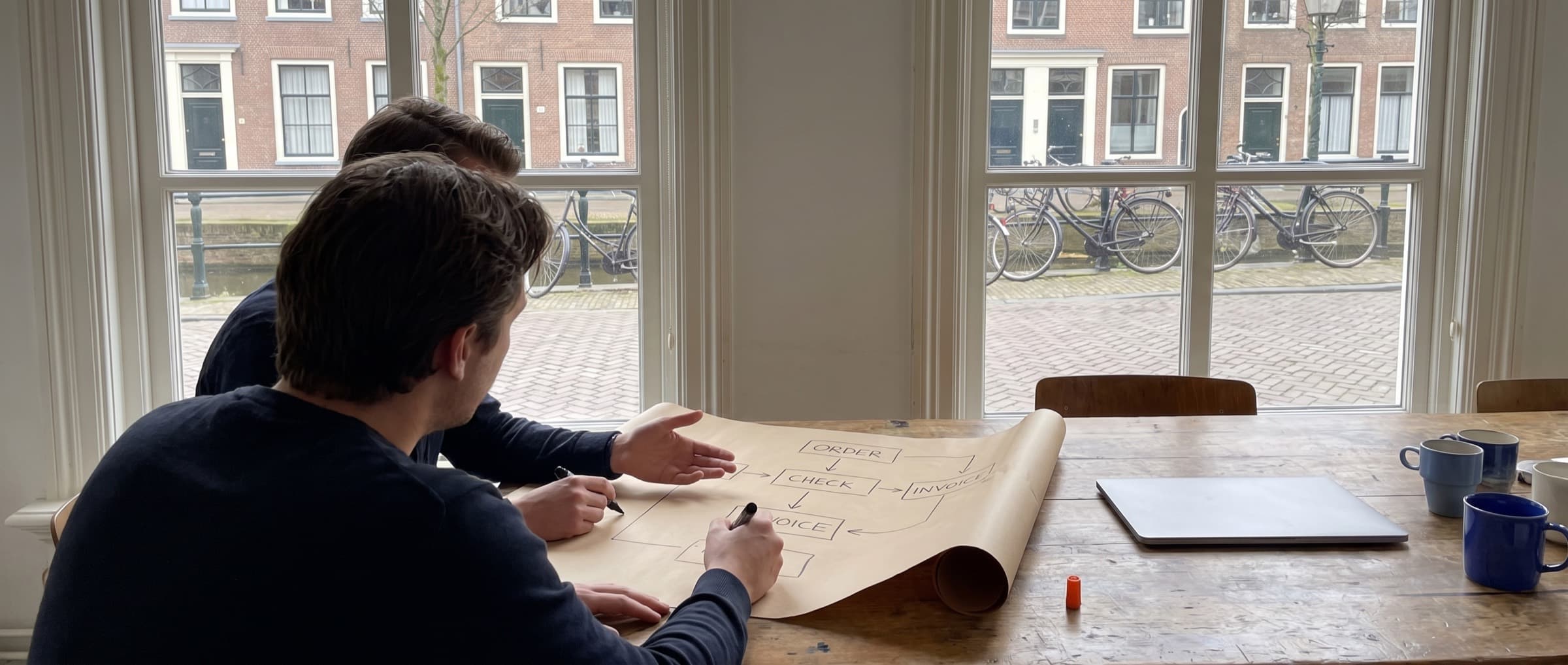 Two colleagues in a Dutch canal-side office sketch a process on paper