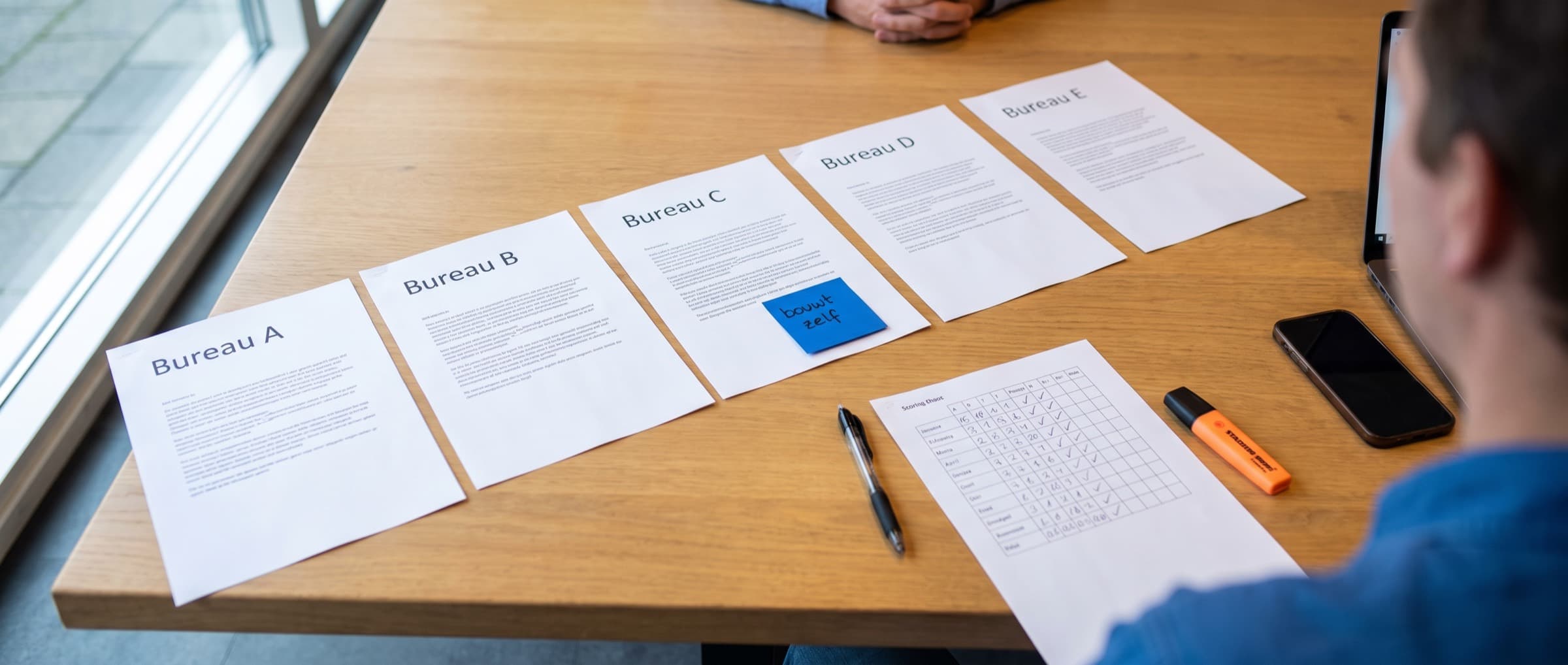 Op een vergadertafel liggen voorstellen van verschillende bureaus naast elkaar
