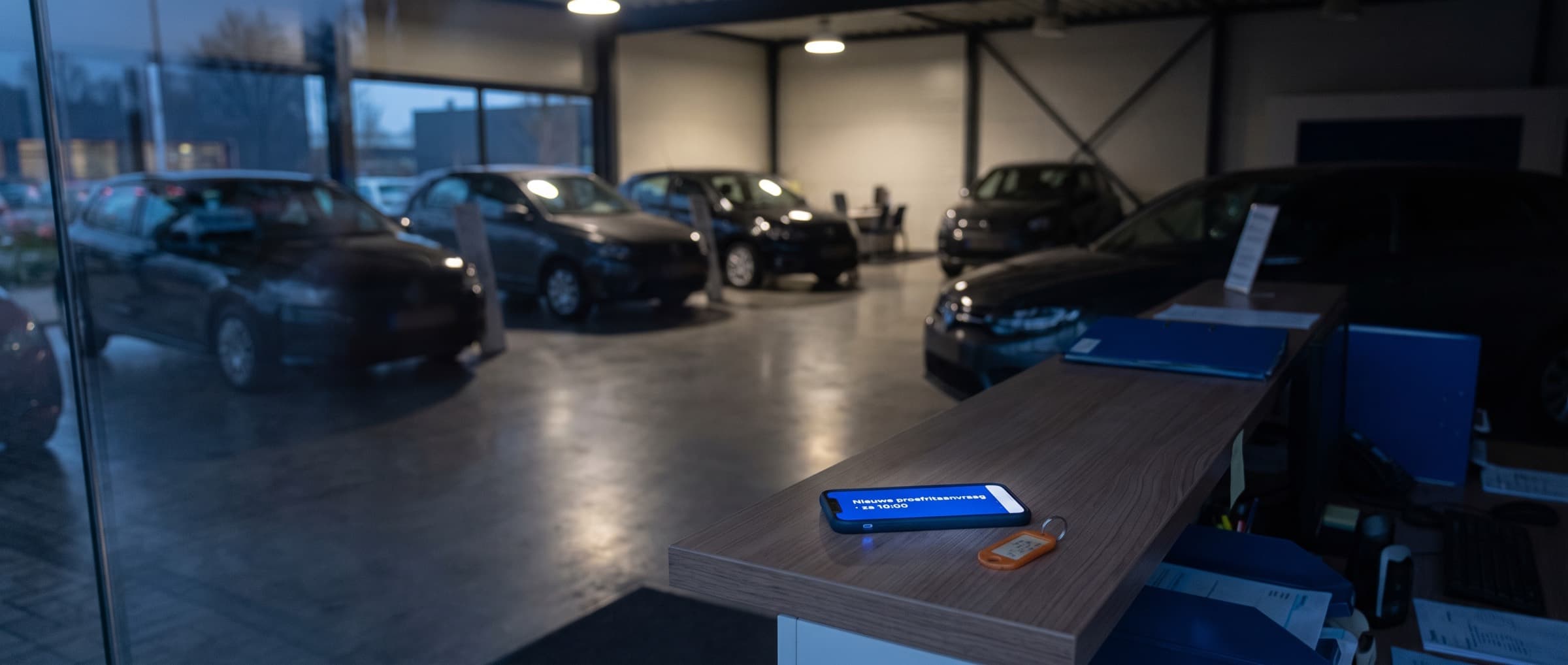 Lege showroom van een autobedrijf in de avond, met een telefoon op de balie waarop net een proefritaanvraag binnenkomt