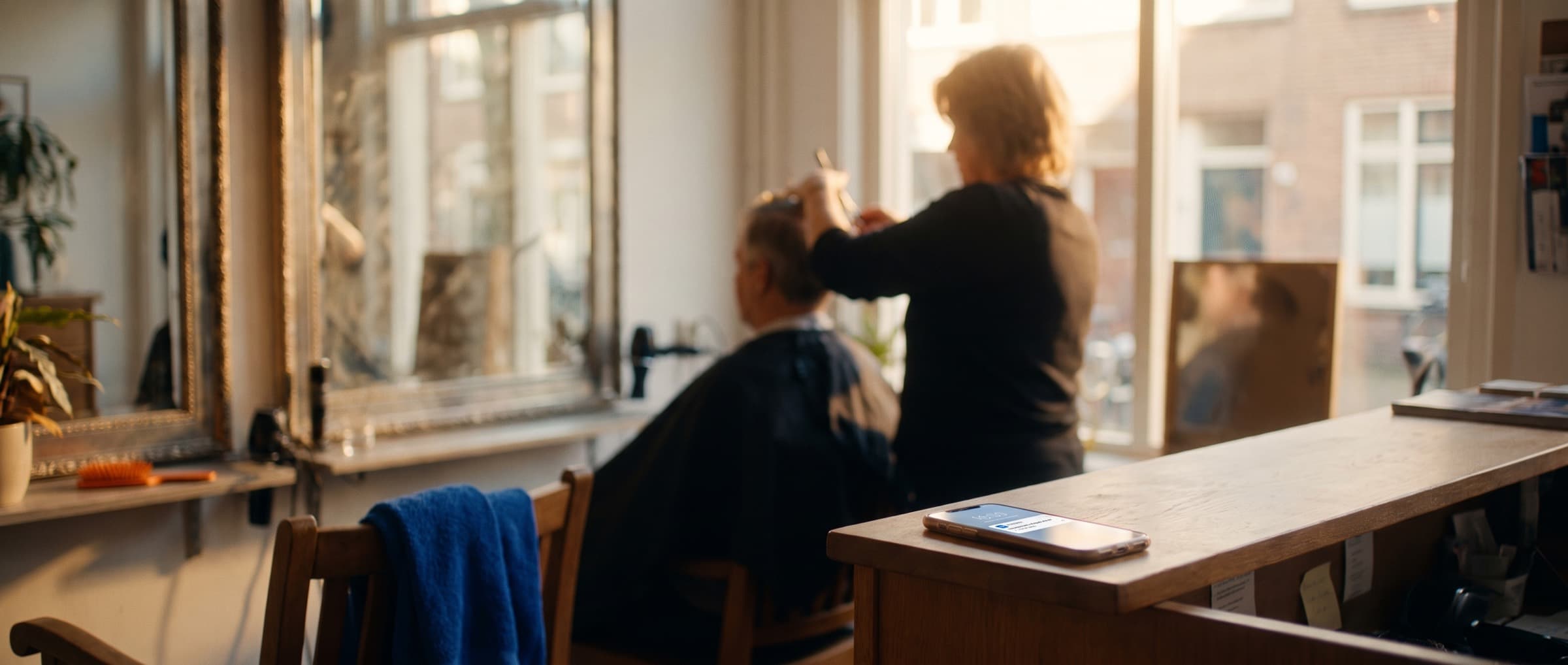 Kapper knipt een klant, op de balie ligt een telefoon met een melding van een nieuwe afspraak