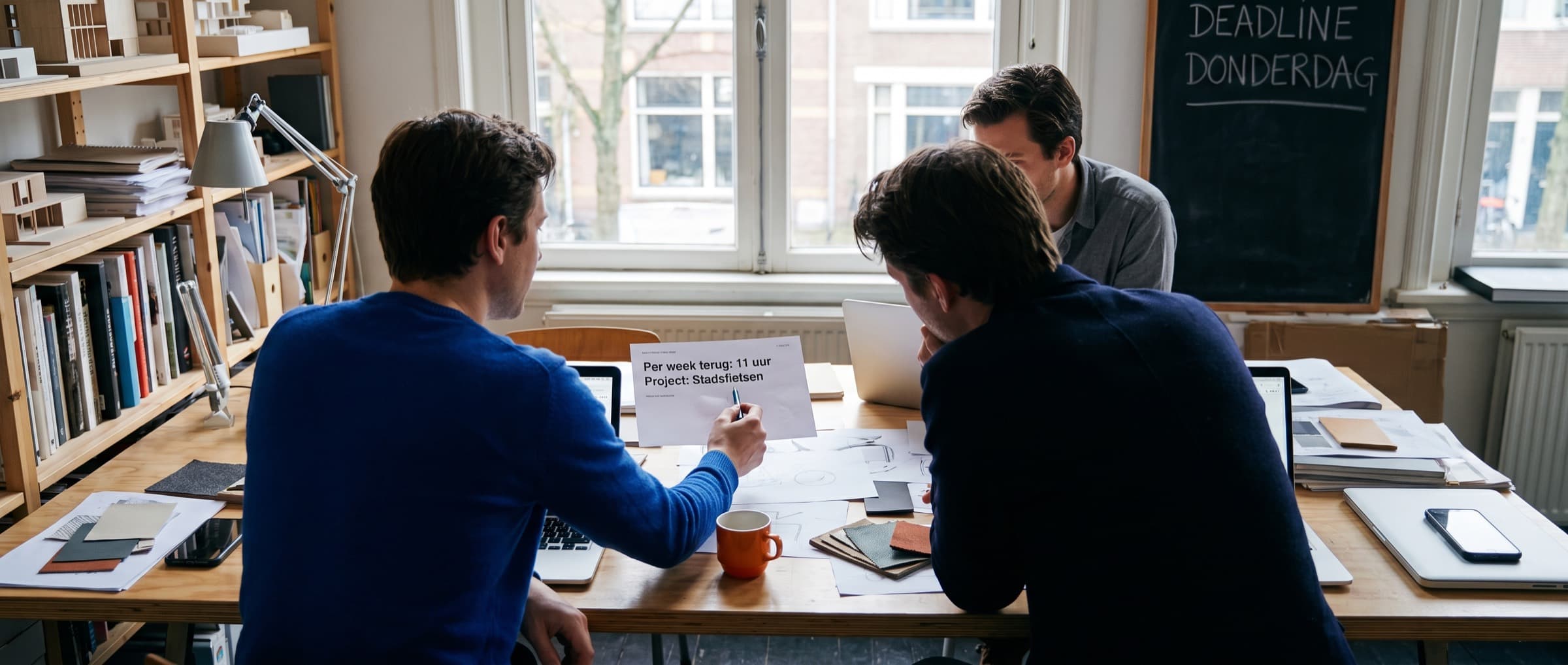 Drie mensen van een kleine studio overleggen aan een gedeelde tafel